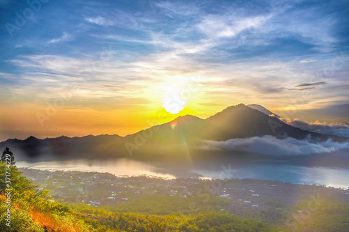 A scenic landscape view of cloud movement during the morning sunrise with golden sunbeam behind the mountain in Bali