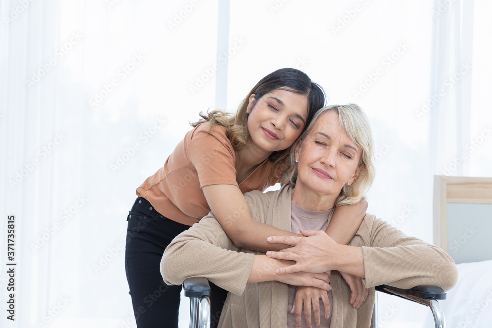 Mother and her adopted daughter hugging each other on a wheelchair with warmth and kindness in the bed room color white.Unusual appearance, diversity, heredity concept. Mother and her adopted daughter hugging each other on a wheelchair with warmth and kindness in the bed room color white.Unusual appearance, diversity, heredity concept.