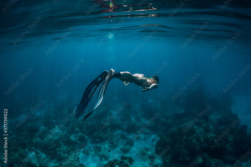 Woman free diver with fins swim underwater in blue ocean Woman free diver with fins swim underwater in blue ocean
