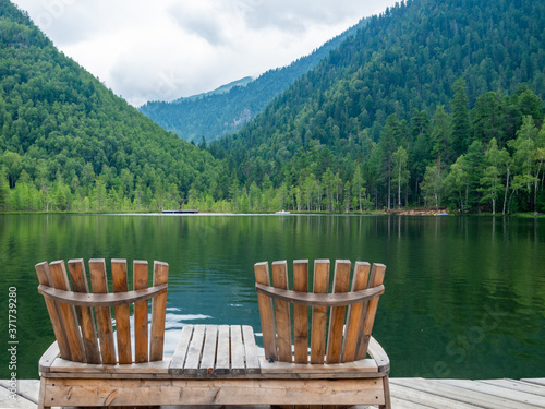 Two comfortable wooden sun loungers against the backdrop of colorful mountains with emerald lake