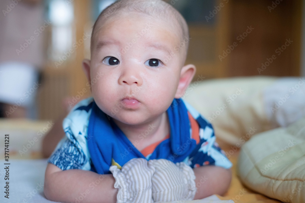 Curious Asian infant baby boy lie on the stomach or prone, wearing white blue clothes on the bed Curious Asian infant baby boy lie on the stomach or prone, wearing white blue clothes on the bed