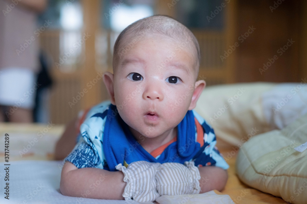 Curious Asian infant baby boy lie on the stomach or prone, wearing white blue clothes on the bed Curious Asian infant baby boy lie on the stomach or prone, wearing white blue clothes on the bed