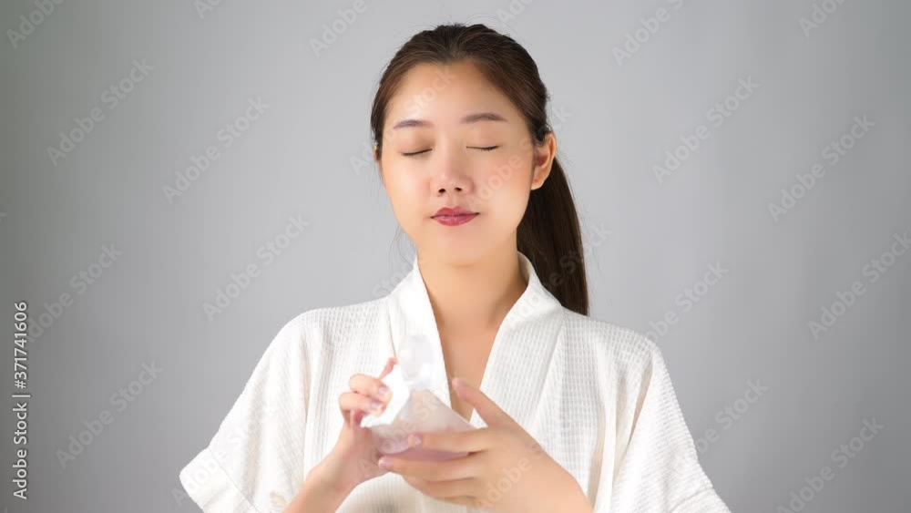 Beautiful young asian woman holding facial cleanser bottle, using cotton pad for applying lotion or cleanser to her beauty face for remove cosmetic. Pretty girl get satisfied with smiley face Beautiful young asian woman holding facial cleanser bottle, using cotton pad for applying lotion or cleanser to her beauty face for remove cosmetic. Pretty girl get satisfied with smiley face
