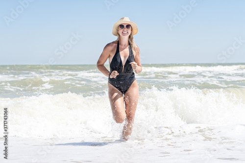 Young sexy woman in black swimsuit and straw hat sunbathes and relaxes on the beach.The girl runs on the waves.