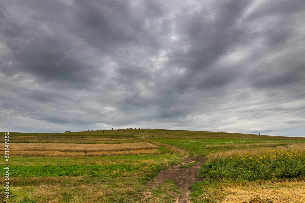 Dirt road leading to the top of a green hill at summertime, gathering storm clouds in the background. Dirt road leading to the top of a green hill at summertime, gathering storm clouds in the background.