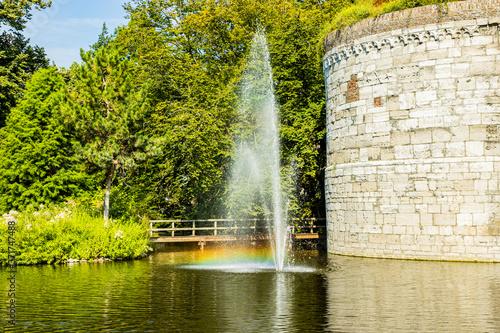 Small fountain with a jet of water reflecting a rainbow in a pond next to the Rondeel (De Vijf Koppen) of the old city wall in the Maastricht city park, sunny day in South Limburg, Netherlands photo