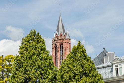 Close-up of the red tower of the Church of Saint John  Sint-Janskerk  among the tops of green leafy trees  sunny day with a blue sky in the city of Maastricht  South Limburg  Netherlands