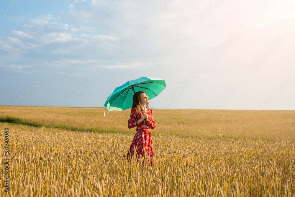 A young woman in a red dress and holding a green umbrella among the golden spikelets in a wheat field. Concept of protection, calmness and freedom A young woman in a red dress and holding a green umbrella among the golden spikelets in a wheat field. Concept of protection, calmness and freedom