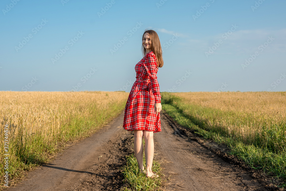 Young pretty woman with freckles in a red dress on the road along a wheat field Young pretty woman with freckles in a red dress on the road along a wheat field