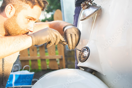 Boy repairs his old motorcycle, taking the horn apart.