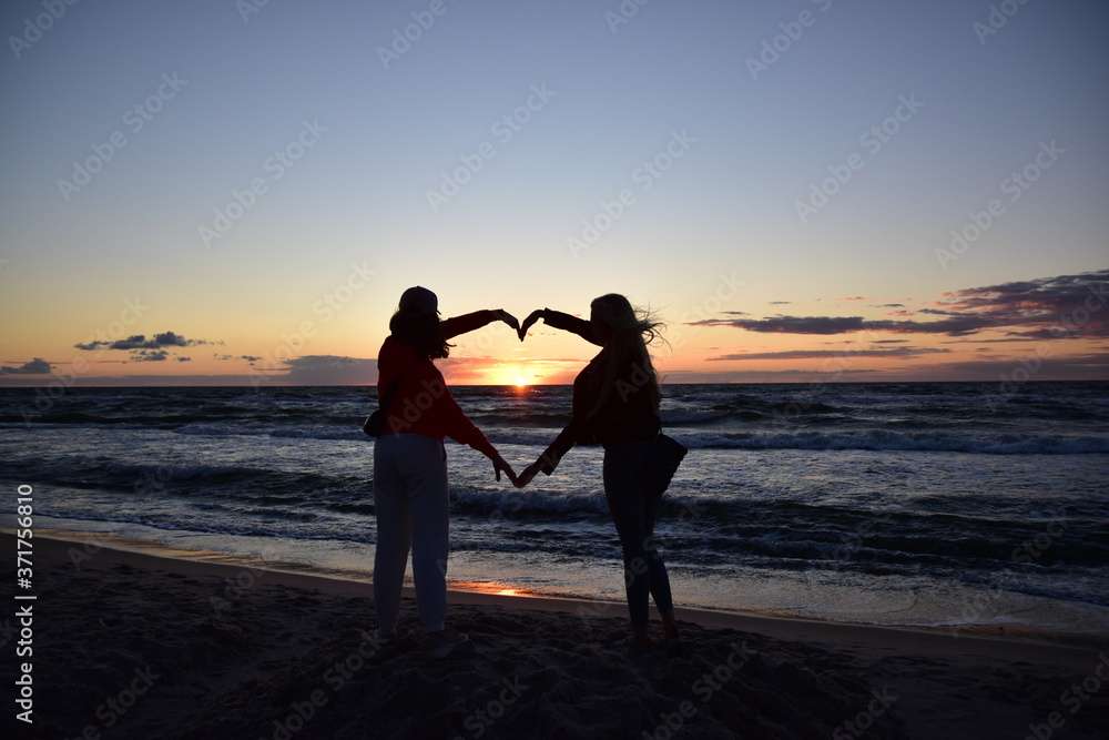 Plakat serce z rąk dwóch osób na tle zachodu słońca na plaży nad morzem ...