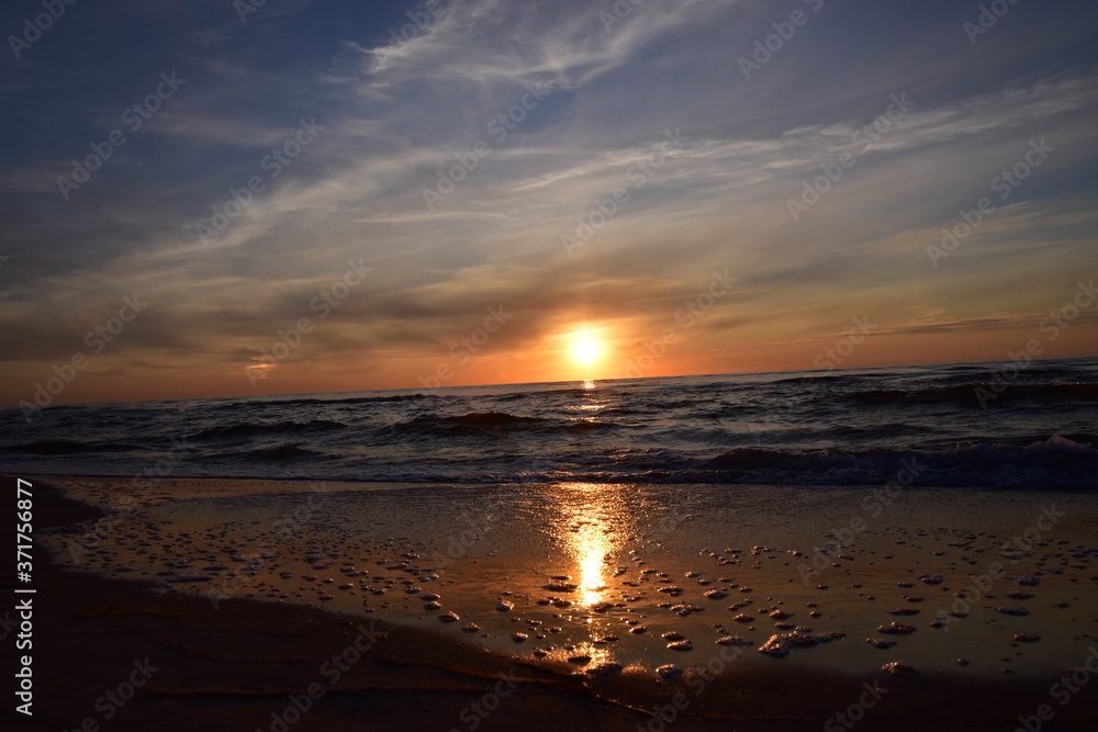 Zachód słońca nad morzem z falami w odcieniach mocnego pomarańczu i czerwieni. 