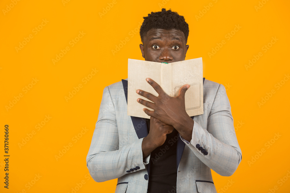 handsome young african male in a jacket reading a book on a yellow background handsome young african male in a jacket reading a book on a yellow background