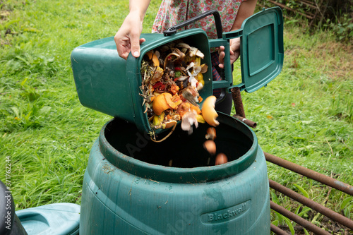 A woman emptying a green home composting bin into an outdoor compost bin to reduce waste photo