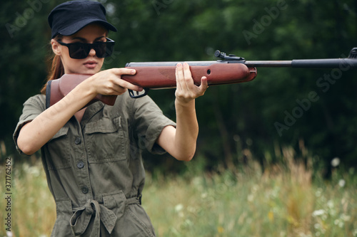 Woman holding a gun aiming sunglasses green leaves 