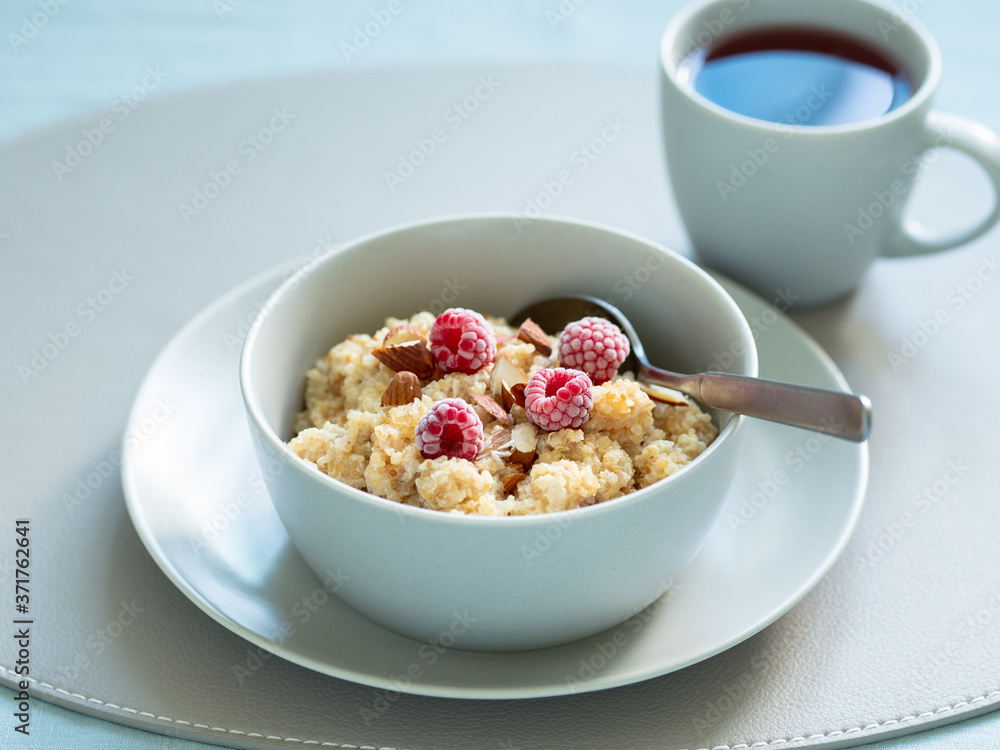 Breakfast with quinoa porrige and cup of hot herbal tea on tabletop. Bowl wit quinoa milk porridge with berries and almond over blue linen tablecloth Breakfast with quinoa porrige and cup of hot herbal tea on tabletop. Bowl wit quinoa milk porridge with berries and almond over blue linen tablecloth