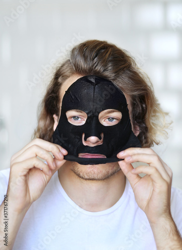  Anti-aging eye therapy. young man taking care of his undereye wrinkles applying facial mask. man moisturizing face mask. Cosmetology and skin care concept.