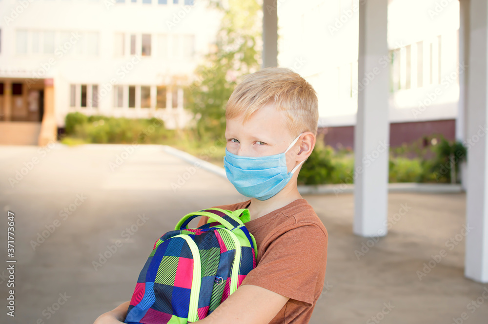 Back to school. School-age boy with a protective medical mask on her on his face with a school backpack. New school year in 2020.C Personal protective equipment. Back to school. School-age boy with a protective medical mask on her on his face with a school backpack. New school year in 2020.C Personal protective equipment.
