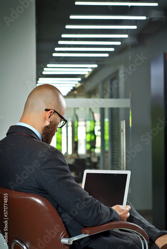 Businessman in a blue shirt sitting in a brown leather chair. Man in a jacket with a laptop in glasses. Bearded office worker at work.