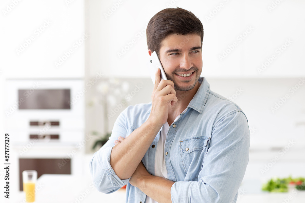 Young handsome man talking on smartphone in the kitchen. Young handsome man talking on smartphone in the kitchen.