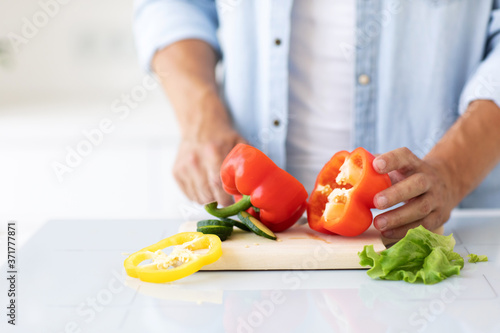 Man cuts red peppers for salad at home kitchen close-up.
