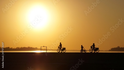 Silhouettes of cyclists leading their bicycles against the setting sun