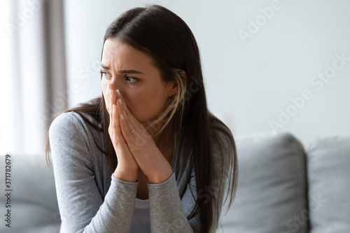Head shot unhappy young woman looking away, feeling doubtful confused about difficult decision. Depressed millennial lady suffering from personal psychological problem, sitting on sofa indoors.
