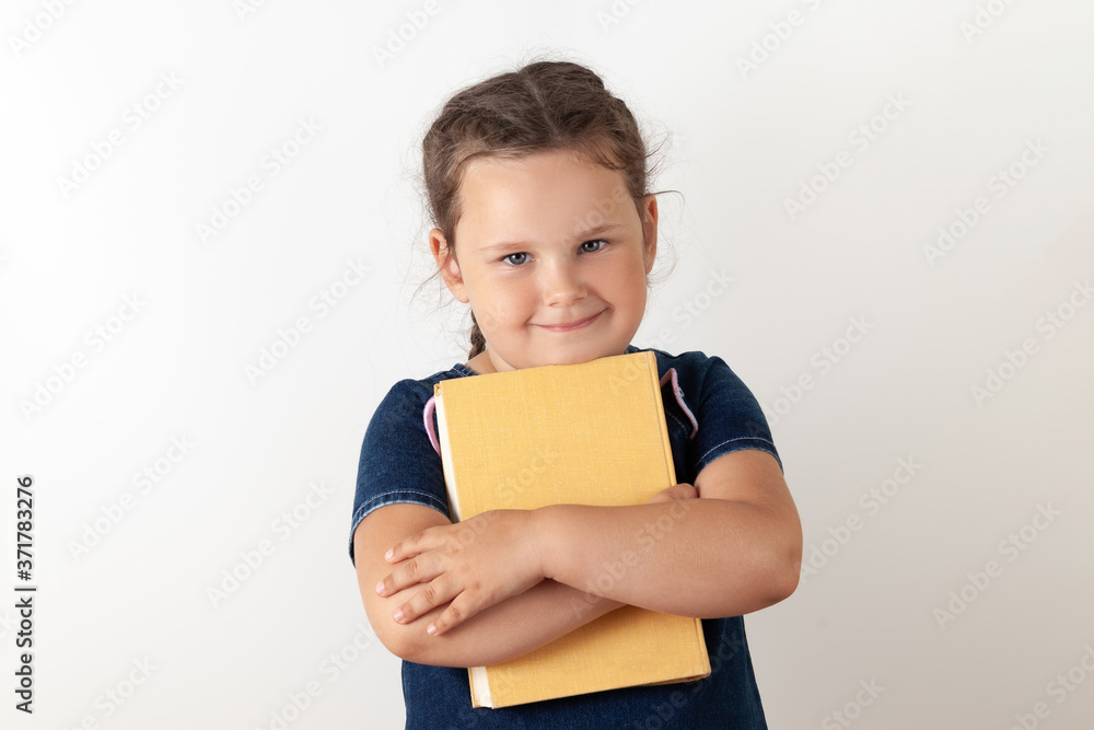 A girl in a blue denim dress holds an orange book in her hands and holds it to her chest, looking up A girl in a blue denim dress holds an orange book in her hands and holds it to her chest, looking up