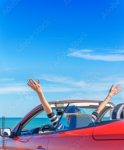 A woman in a red car raised her hands up at the seaside.