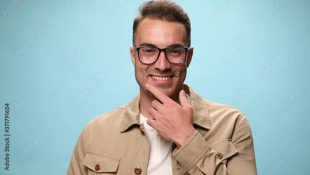 attractive casual man arranging his jacket, smiling, touching his chin, crossing his arms, looking aside on blue background attractive casual man arranging his jacket, smiling, touching his chin, crossing his arms, looking aside on blue background