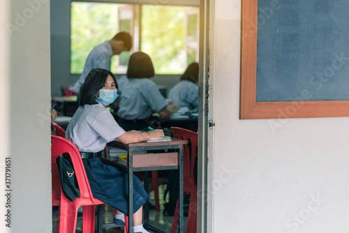 An Asian female high school student wearing a mask is sitting in the classroom during the Coronavirus 2019 (Covid-19) epidemic.