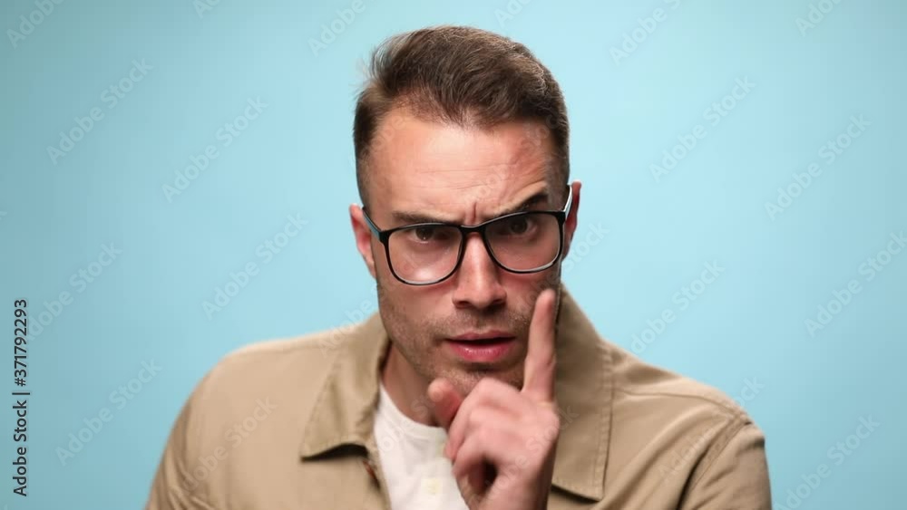 handsome casual guy being irritated and asking for silence, gesturing a shut up sign on blue background handsome casual guy being irritated and asking for silence, gesturing a shut up sign on blue background