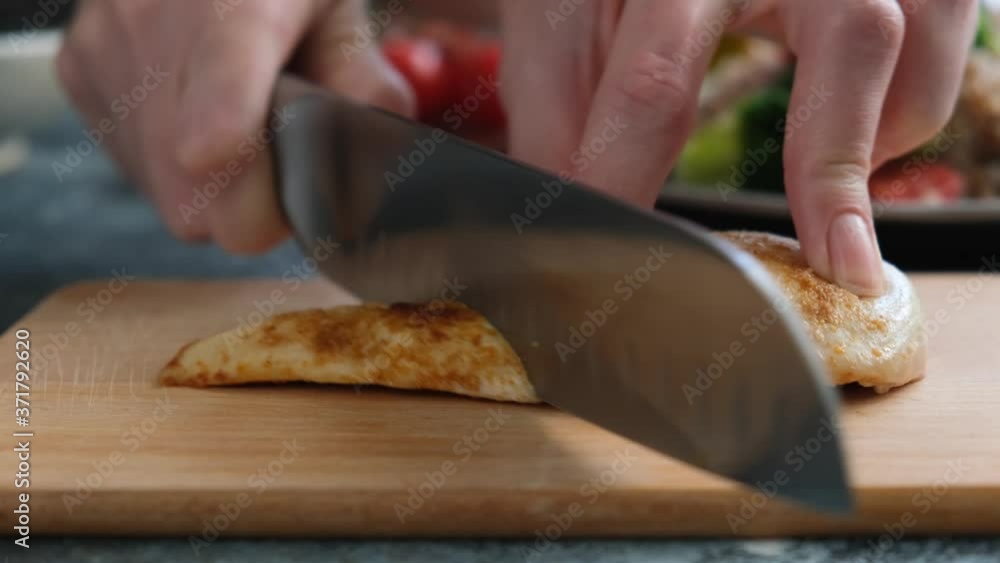 Cutting juicy grilled chicken breast on a wooden cutting board, closeup view Cutting juicy grilled chicken breast on a wooden cutting board, closeup view
