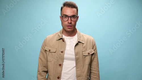 attractive casual guy making worries, being shocked, slapping his face, puffing cheeks and can't explain what's happening on blue background