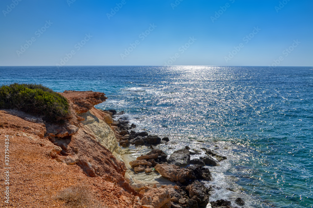View of the blue water of the Mediterranean Sea and coastal cliffs on the coast of the island of Cyprus. Sunny hot day at the coastline near the town of Paphos.