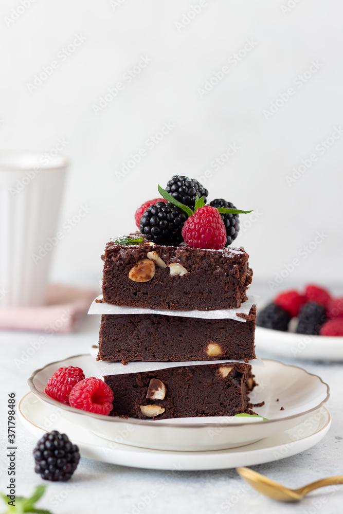 pieces of fresh chocolate brownie with hazelnuts, raspberries and blackberries. American traditional delicious dessert. Gray background. vertical image pieces of fresh chocolate brownie with hazelnuts, raspberries and blackberries. American traditional delicious dessert. Gray background. vertical image