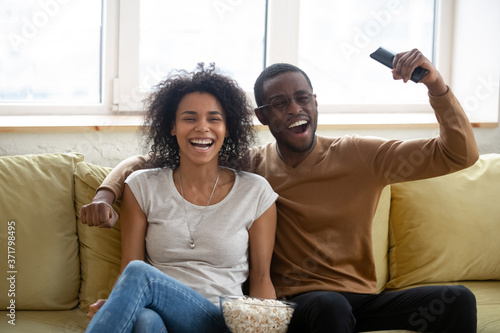 We score. Happy excited young black family husband and wife sitting on sofa watching sport competition by digital cable channel, african couple in love enjoying soccer match online by smart tv at home photo
