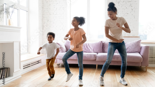 Active leisure together with kids. Millennial african mother teaching school age daugter and little son modern dance movements  black boy and girl spend time at dancing with young babysitter at home