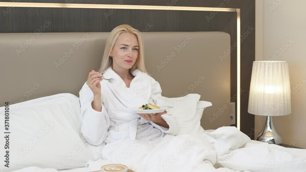 Attractive lady enjoy breakfast in hotel, blonde lady in bathrobe sit on bed and have meal in morning, relax. Attractive lady enjoy breakfast in hotel, blonde lady in bathrobe sit on bed and have meal in morning, relax.