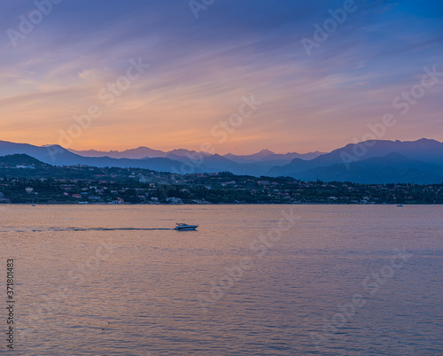 A boat in the sunset with the silhouettes of the mountains in the background on Lake Garda, Italy © Julia Hermann