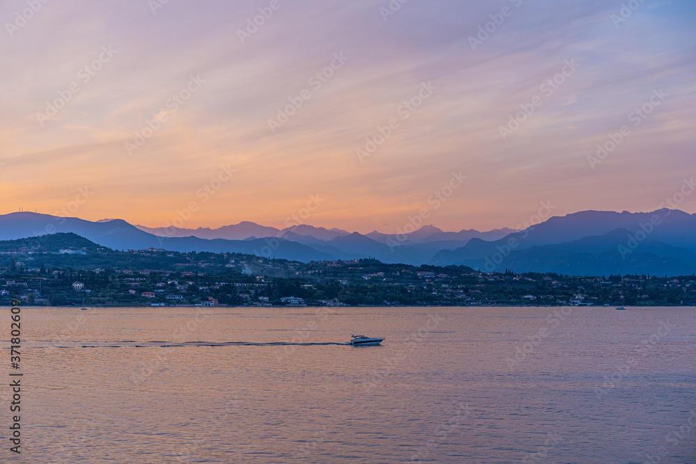 Fototapeta premium A boat in the sunset with the silhouettes of the mountains in the background on Lake Garda, Italy