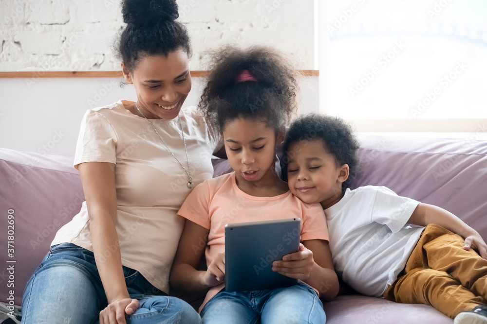 Happy learning. Millennial african mother and two little children daughter and son sitting on comfy couch at home studying foreign language online on digital pad, using education app on tablet pc