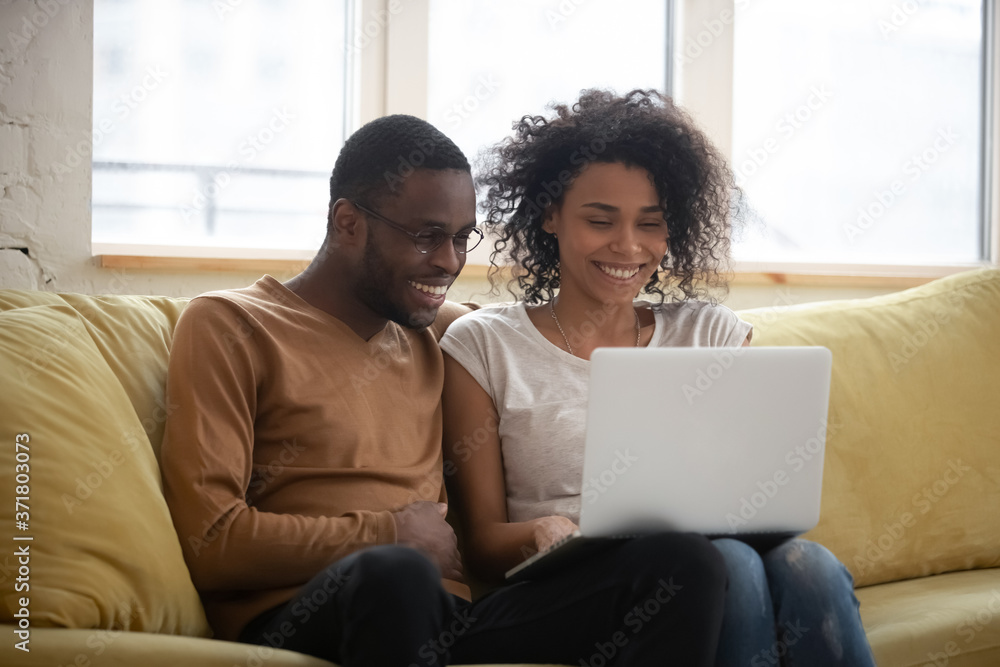 Happy black couple speak with friends online making video call. Smiling mixed race married man and woman sitting on coach in living room use laptop for distance conference calling Happy black couple speak with friends online making video call. Smiling mixed race married man and woman sitting on coach in living room use laptop for distance conference calling