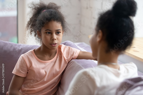 Sharing secrets with mom. Preteen african girl sitting on couch having confident frank talk with understanding mother or elder sister, school psychologist listening to bullying or racial abuse victim