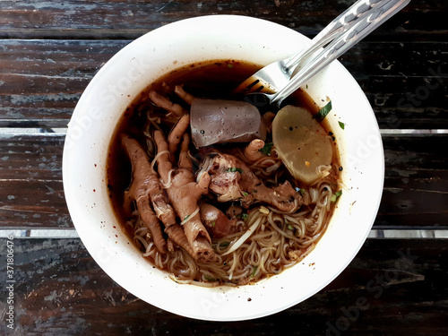 A bowl of noodle soup with chicken drumstick and chicken feet on wooden table