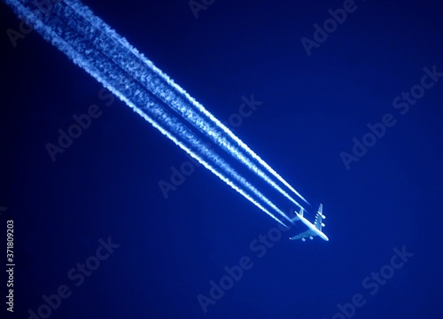Awesome white jet trails in a dark blue sky and a white airplane 