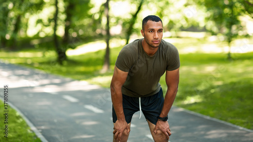 Handsome African American jogger resting during his morning run at summer park, free space