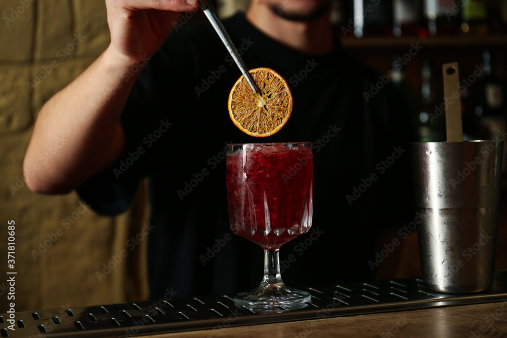 Bartender decorating glass of fresh alcoholic cocktail at bar counter, closeup