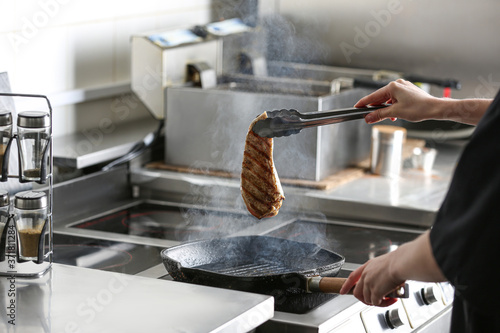Female chef cooking chicken fillet on stove in restaurant kitchen, closeup