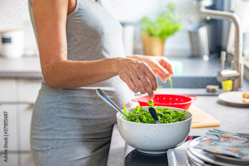 Pregnant woman preparing healthy vegan food in a white salad bowl